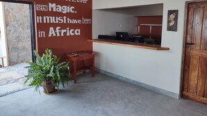 Un espace d’accueil avec un mur en pierre, un bureau en bois, une plante en pot et une porte en bois.