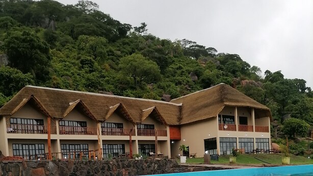 Un complexe hôtelier doté d’une piscine, de bâtiments aux toits de chaume et entouré d’une végétation luxuriante.