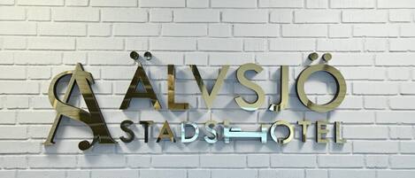 Un letrero de hotel con el nombre 'Alvsjö Stadshotel' en letras metálicas sobre una pared de ladrillo blanco.