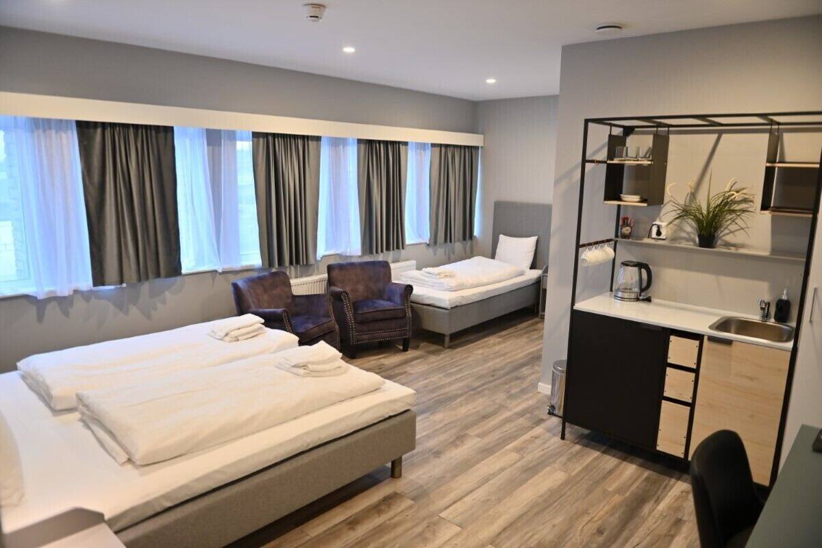 A hotel room with two beds, a small kitchenette, a seating area, and a large window with curtains.