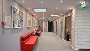 A hallway with a red bench, artwork on the walls, and a white brick accent wall. - Älvsjö stadshotell (Arsta)