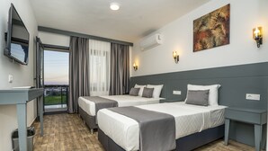 Ein Hotelzimmer mit zwei Betten, einem Schreibtisch, einem Stuhl, einem Fernseher und einem Balkon mit Vorhängen.