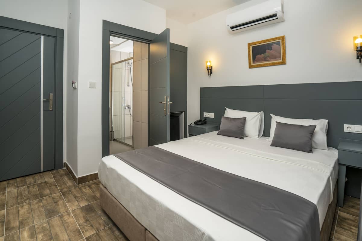 Quarto de hotel com uma cama grande, uma mesa de cabeceira, ar condicionado fixado na parede e uma porta para um banheiro.