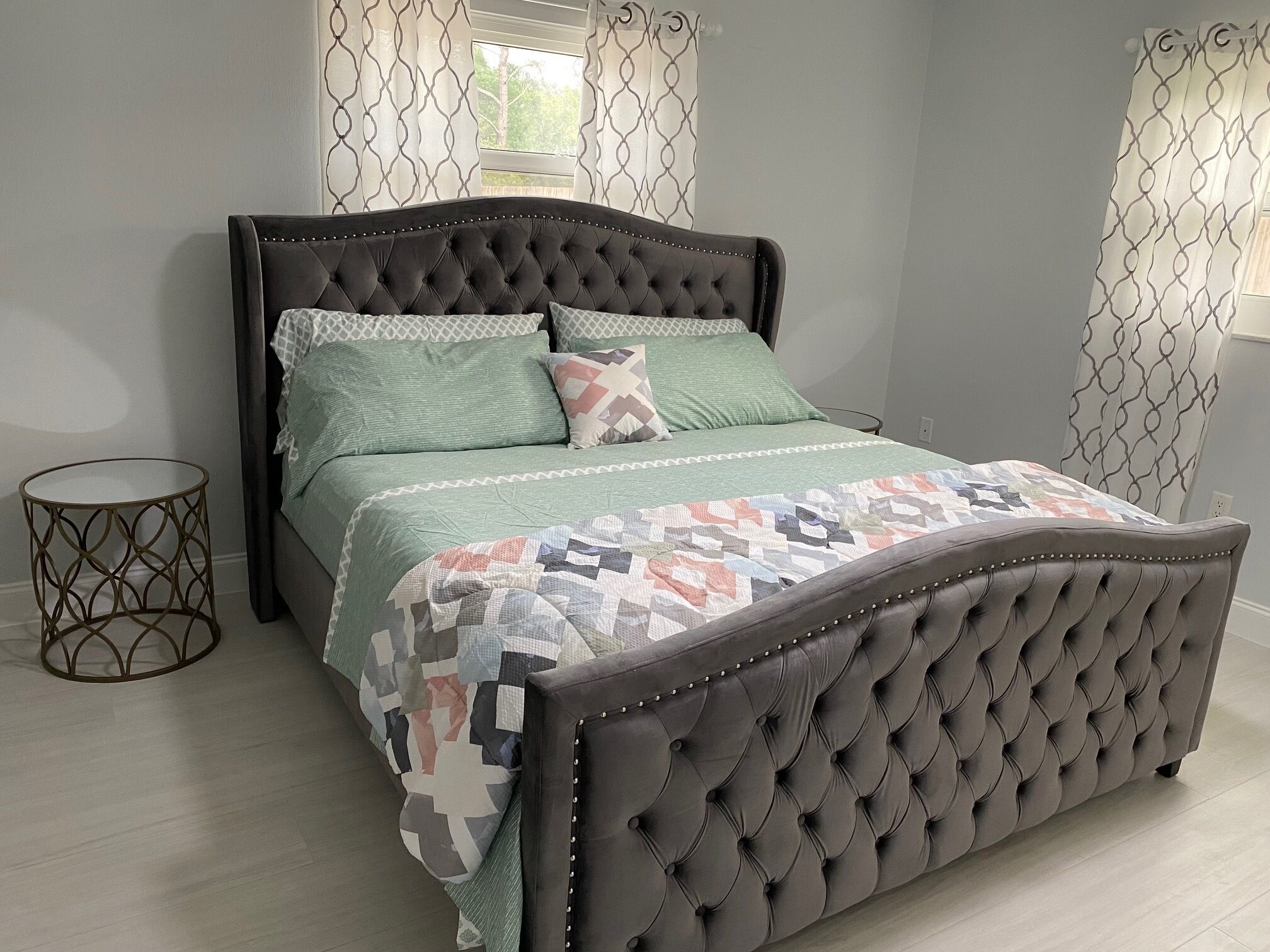 A bedroom with a tufted headboard, a green bedspread, and patterned pillows.