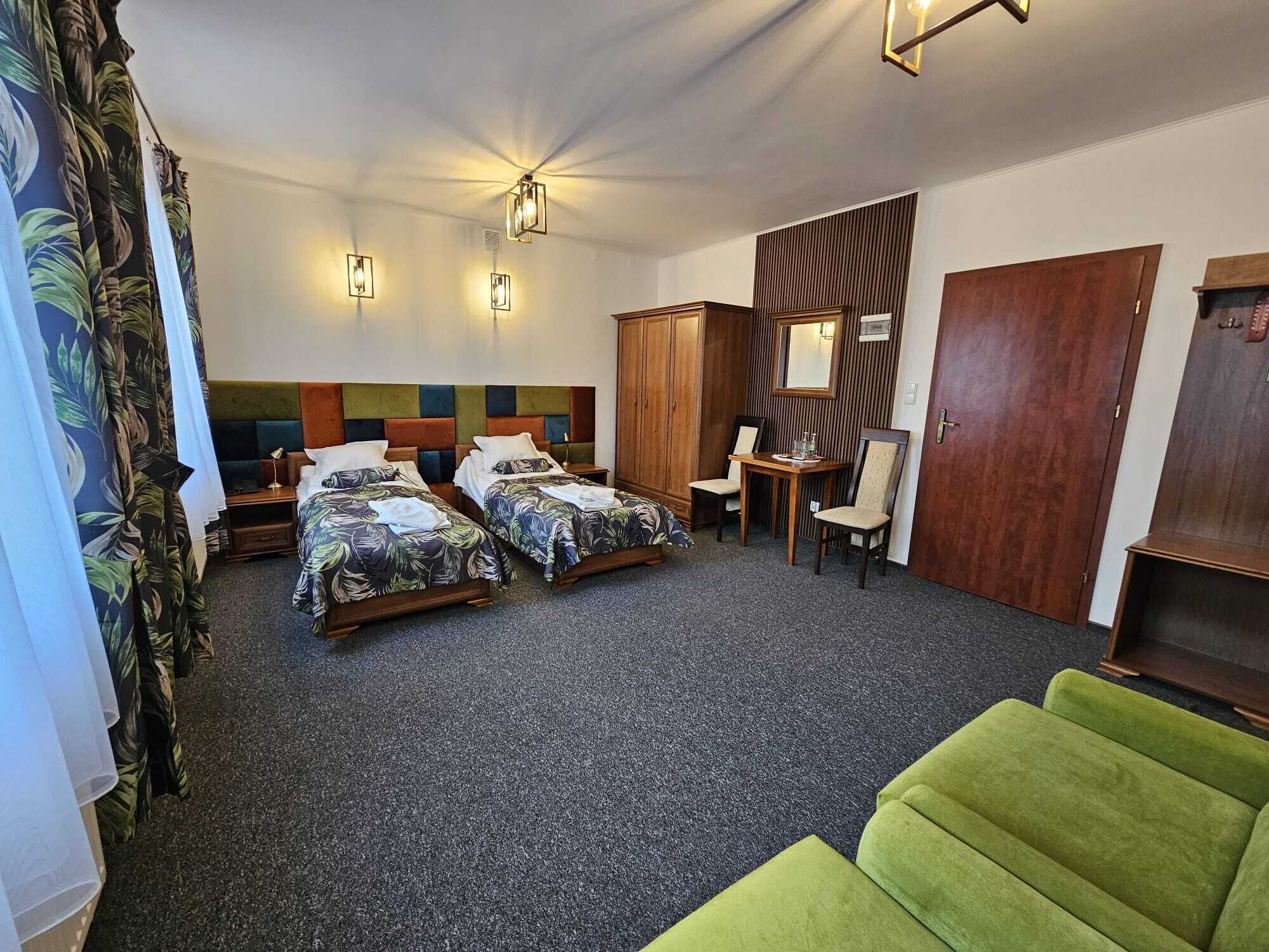 Habitación de hotel con dos camas, una mesita, una silla, un armario y un sofá verde.