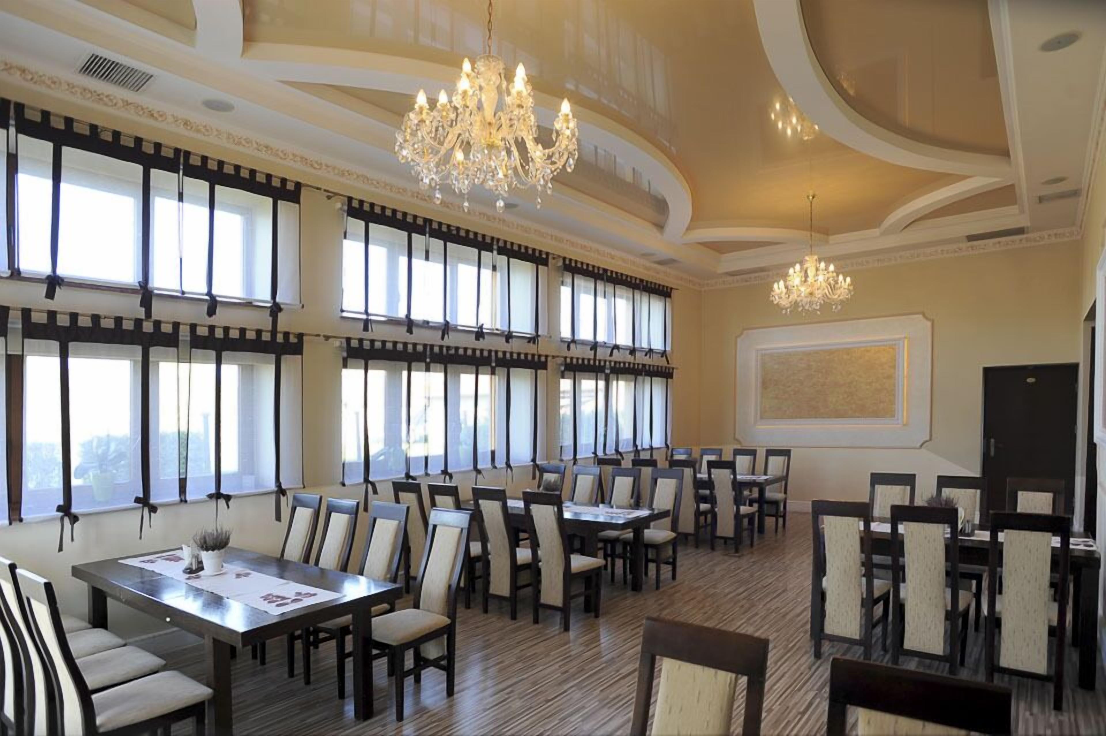A spacious dining area with multiple tables and chairs, large windows, and chandeliers.