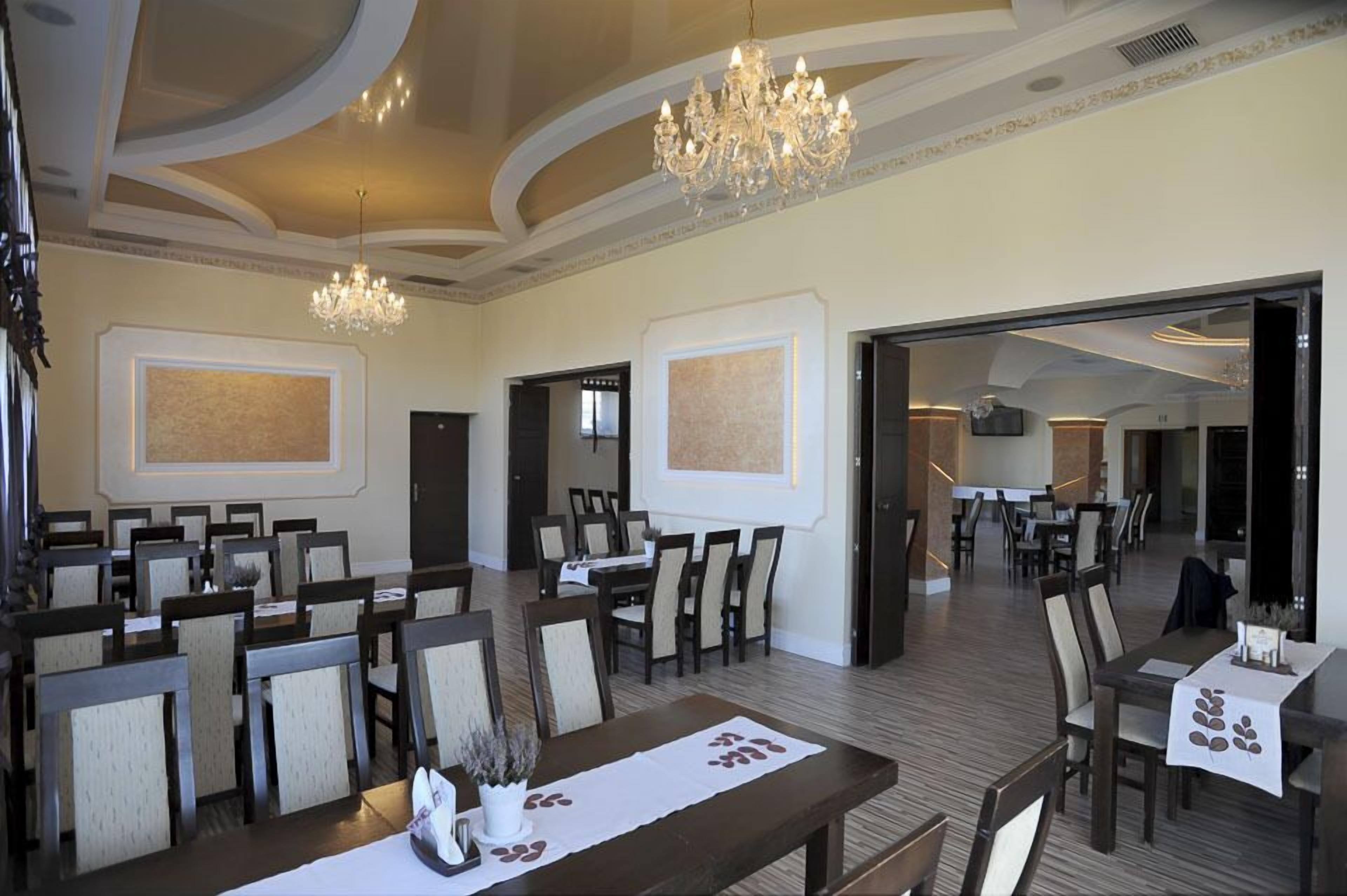 Un amplio comedor con múltiples mesas y sillas, una araña y obras de arte enmarcadas en las paredes.