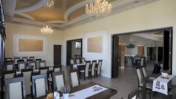 Un amplio comedor con múltiples mesas y sillas, una araña y obras de arte enmarcadas en las paredes.