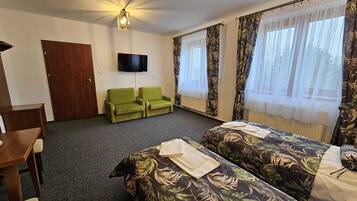 Habitación de hotel con dos camas individuales, un televisor, una puerta de madera y sillones verdes.