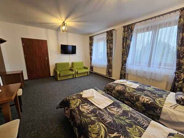 Habitación de hotel con dos camas individuales, un televisor, una puerta de madera y sillones verdes.