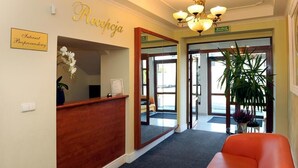A reception area with a wooden reception desk, a sign reading "Reception," a mirror, and a potted plant. - Restauracja Hotel Imperial (Jaslo)