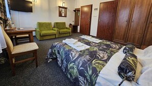 A hotel room with a bed, two green chairs, a wooden desk, a flat-screen TV, and a wardrobe. - Restauracja Hotel Imperial (Jaslo)