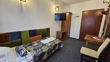 A hotel room with a bed, a desk, a chair, a TV, and a wardrobe.