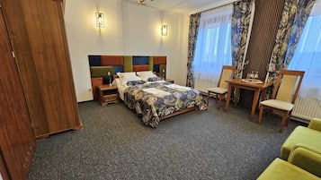 A hotel room with a bed, a desk, a chair, a wardrobe, and a window with curtains.