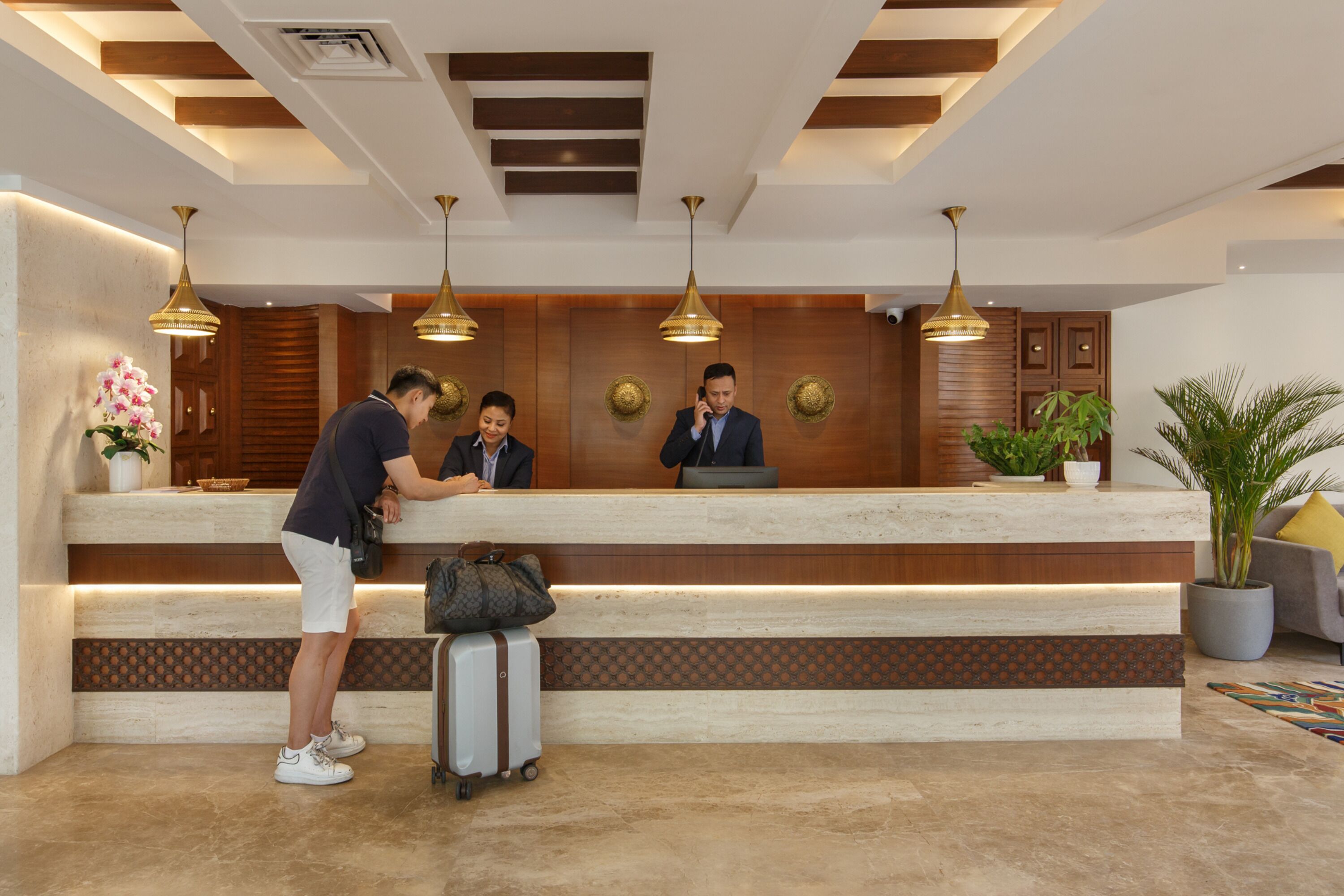 Ein Hotel-Empfangsbereich mit Marmor-Theke, drei Mitarbeitern und einem Gast.