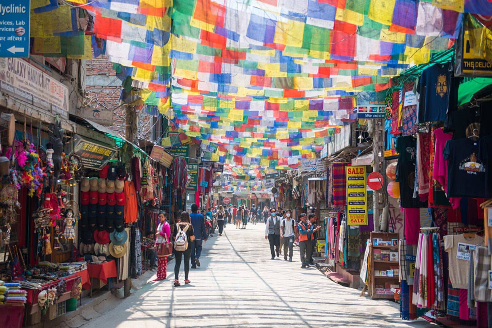 A bustling market street with colorful flags hanging overhead and various shops on either side.