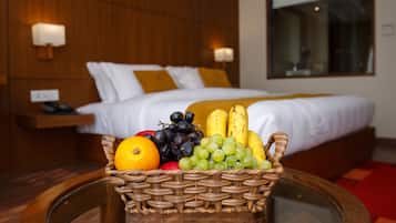 Habitación de hotel con cama, mesita de noche, cesta de mimbre con fruta y una mesa de vidrio.