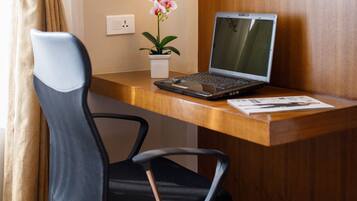 Een laptop op een houten bureau, met een stoel, een potorkidee en een stopcontact aan de muur.