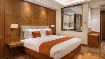 A modern hotel room with a large bed, wooden paneling, a mirror, and a small bathroom area.