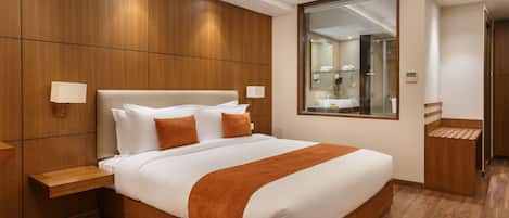 Una habitación de hotel moderna con una cama grande, paneles de madera, un espejo y un pequeño baño.