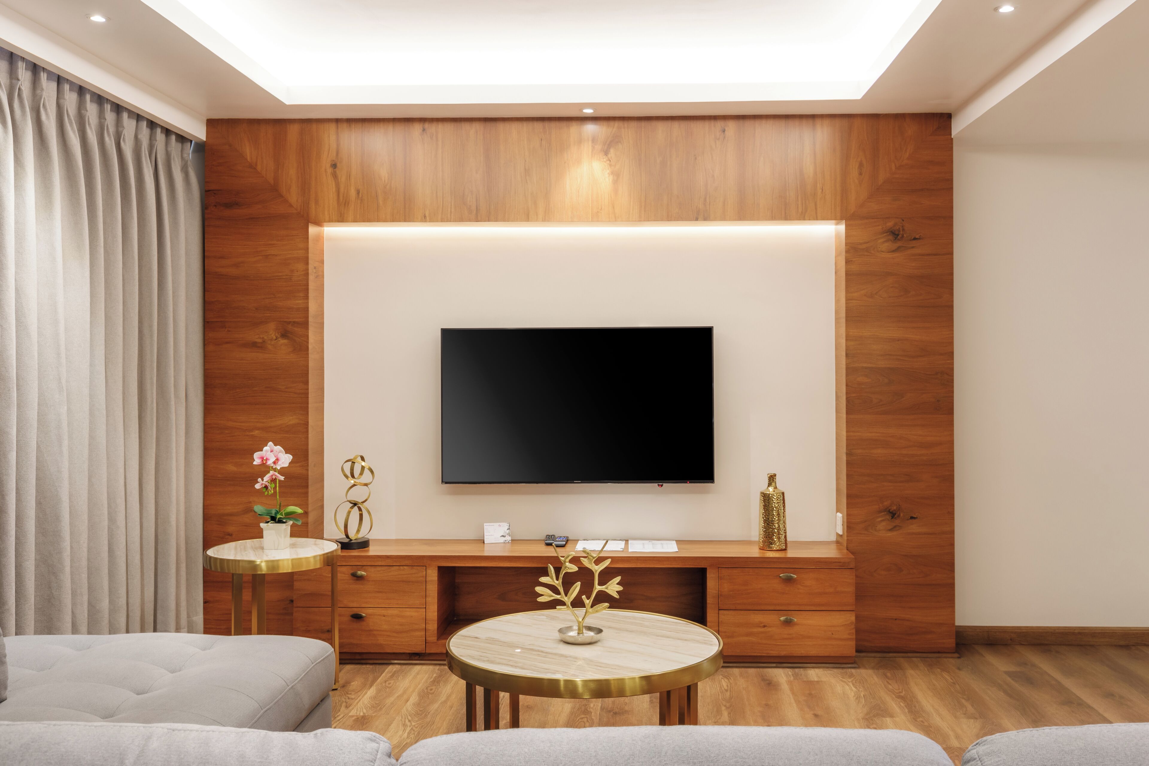 Una sala de estar moderna con una televisión de pantalla plana montada en una pared de madera, una mesa de centro redonda, un sofá y una mesita auxiliar con un jarrón.