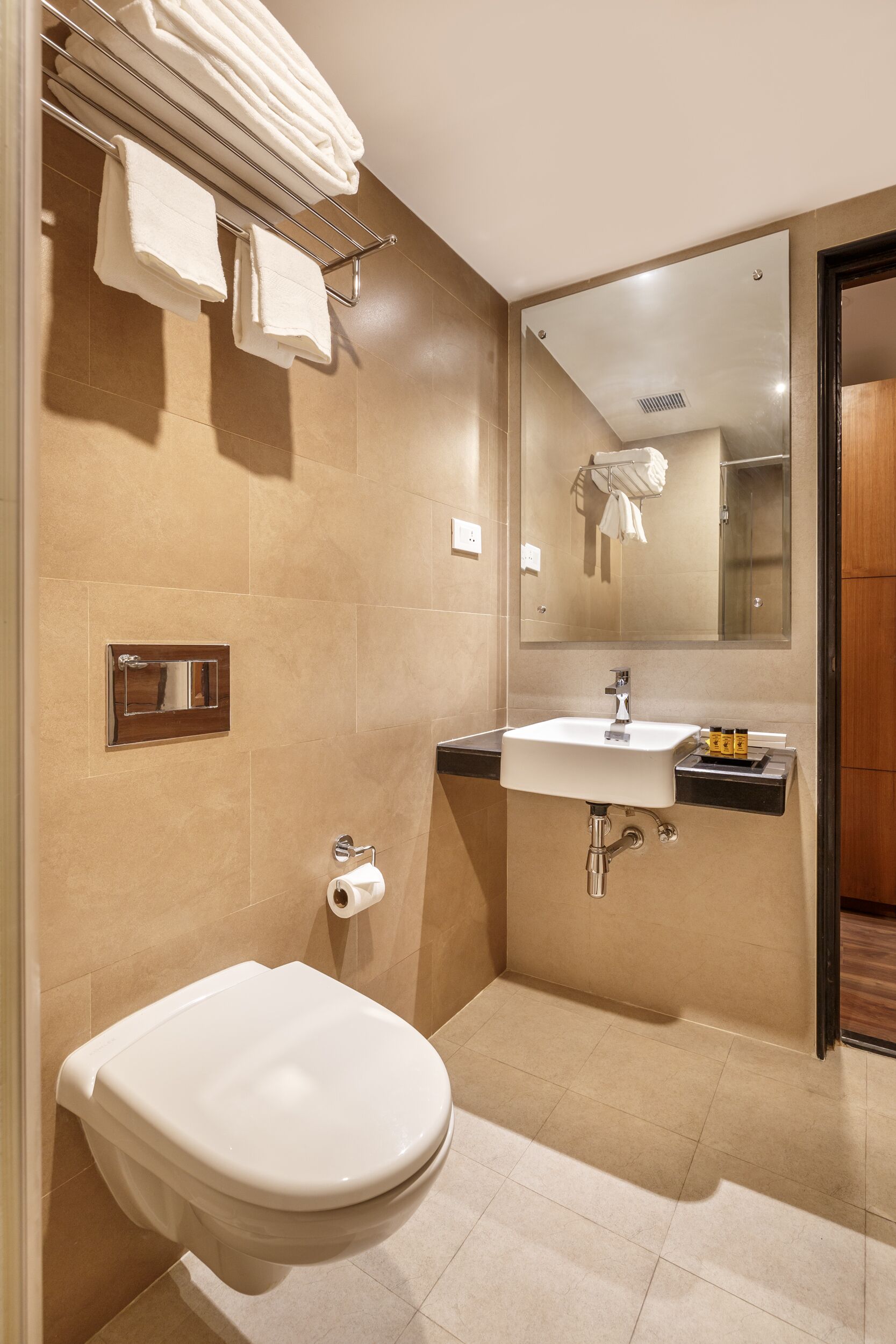 A modern bathroom with a white sink, mirror, and toilet. There are towels hanging on a rack and a toilet paper holder on the wall.