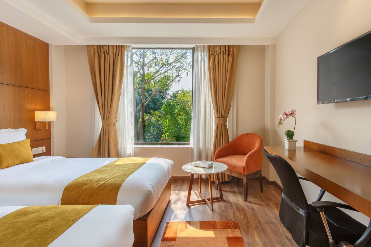 A hotel room with two beds, a desk, a chair, a TV, and a window with curtains.