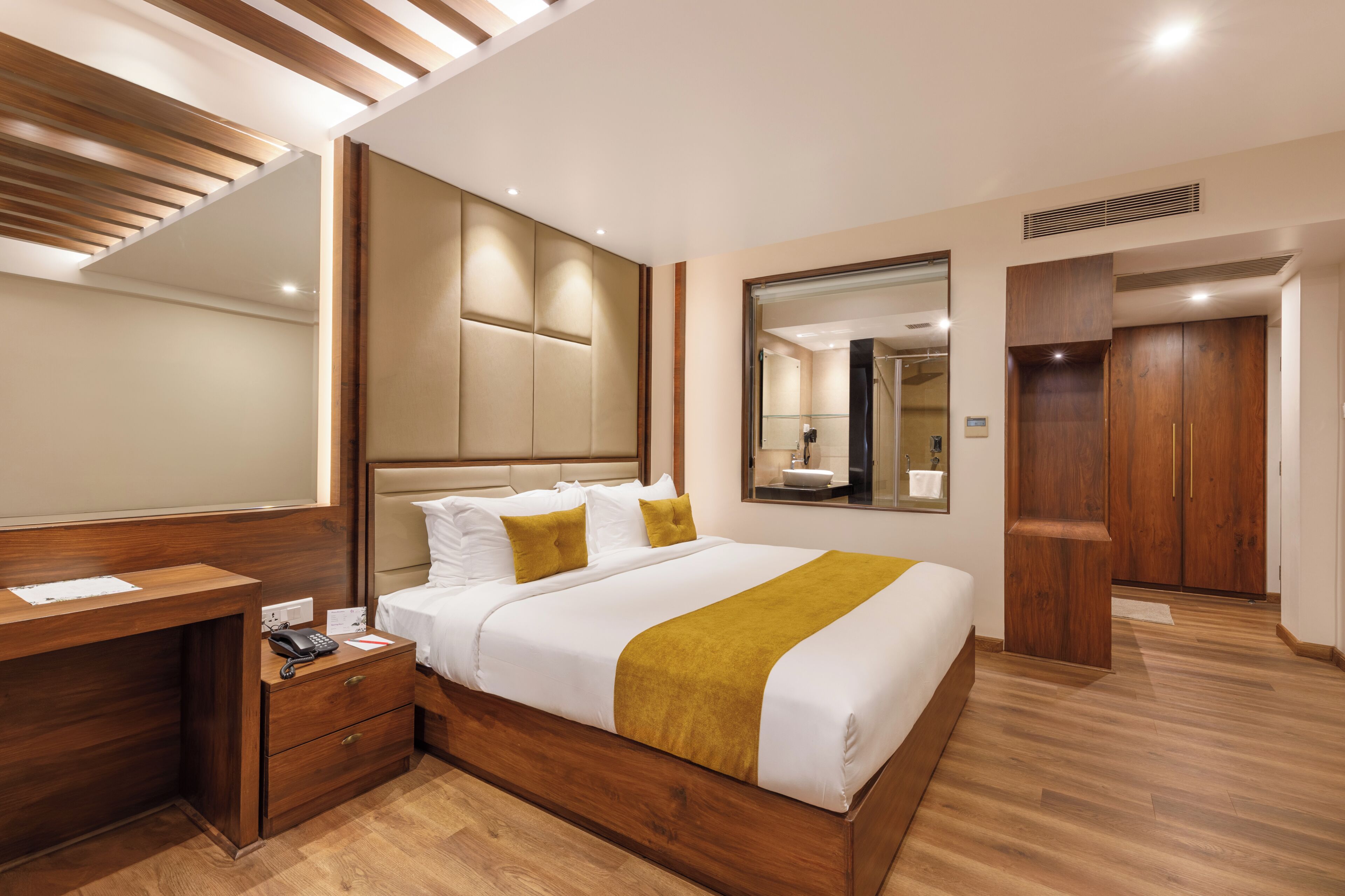 Une chambre d’hôtel moderne avec un lit en bois, un bureau, un grand miroir et une armoire.