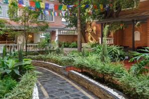 A courtyard with a brick wall, a statue, and various plants. - Hotel Thrive, A Tropical Courtyard (Kathmandu)