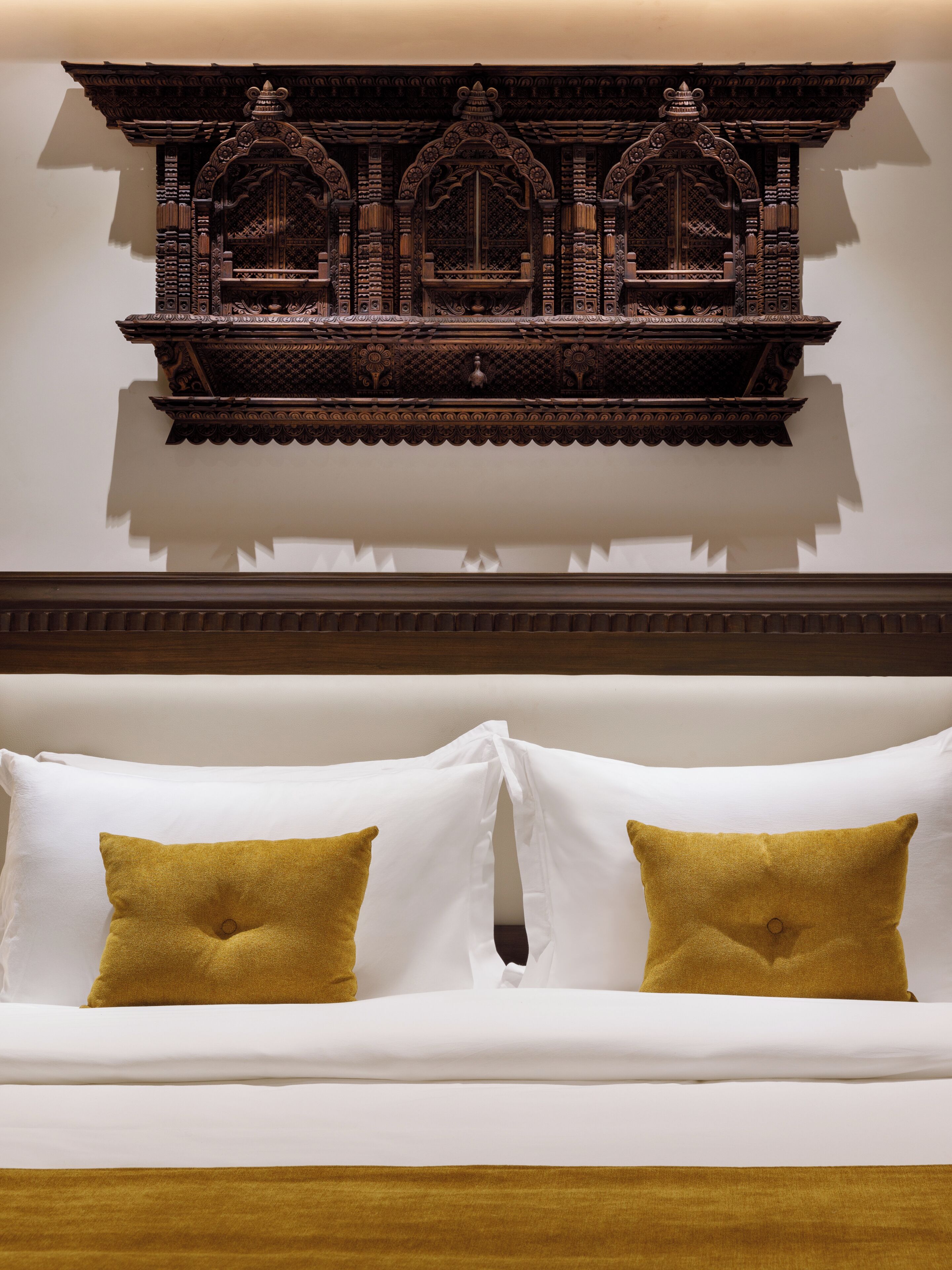 A bed with white and mustard pillows, a wooden headboard, and an ornate wall decoration above.