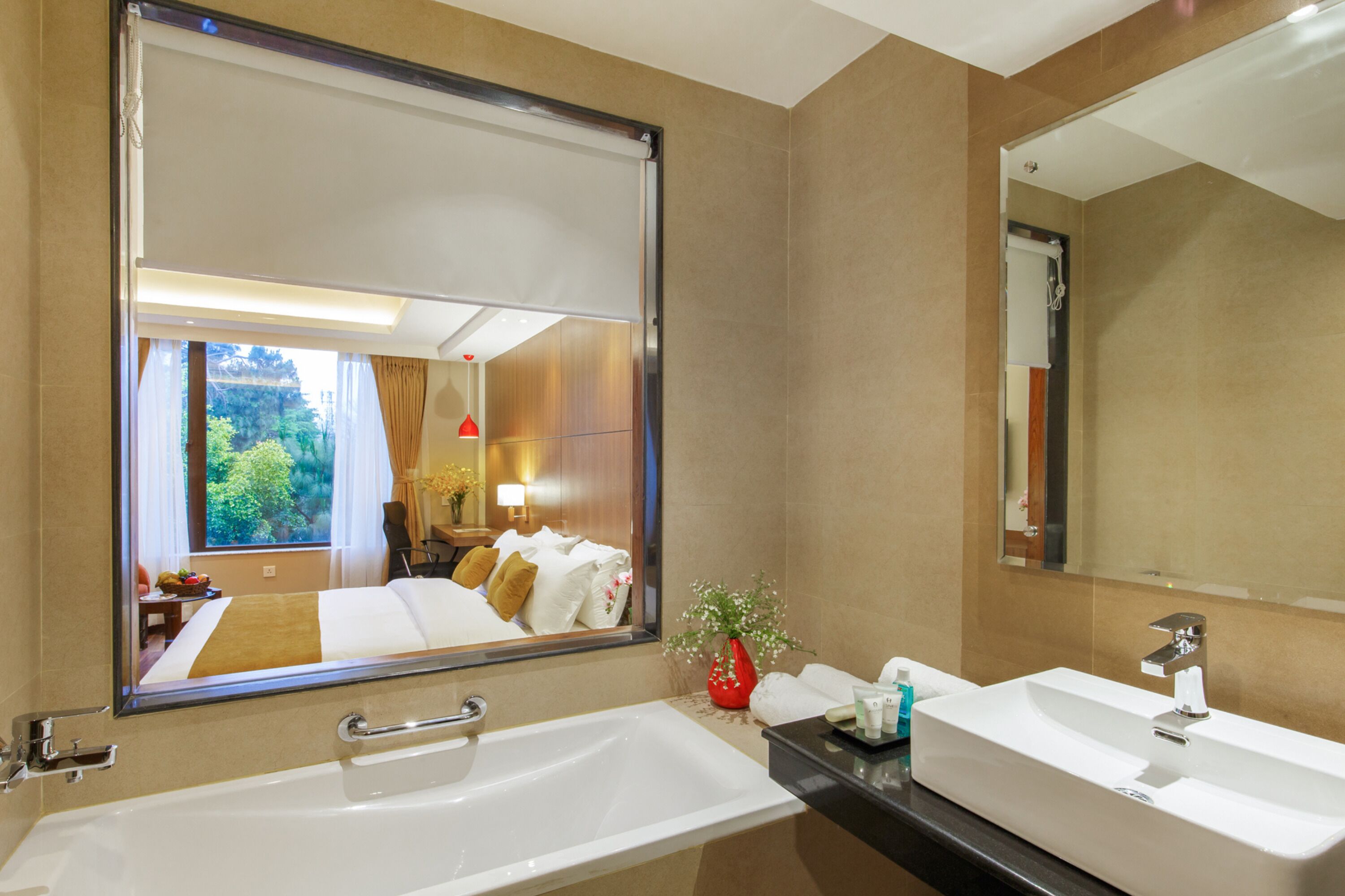 A hotel bathroom with a large mirror, a bathtub, a sink, and a window with curtains.