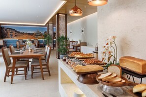 A restaurant with a buffet setup, including bread and pastries, and a view of a cityscape through the window. - Hotel Thrive, A Tropical Courtyard (Kathmandu)