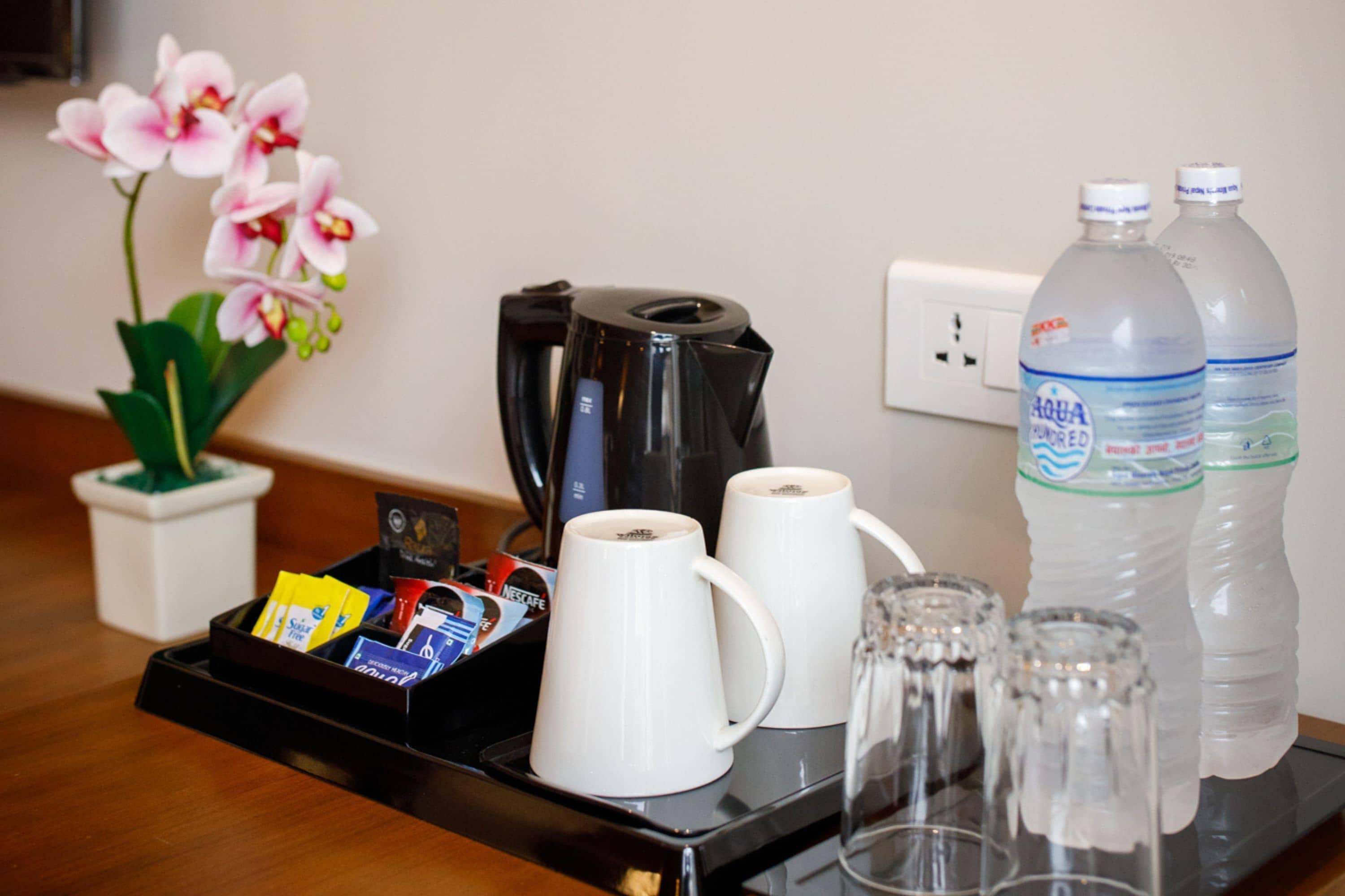 A tray with coffee mugs, a coffee maker, and water bottles on a table.