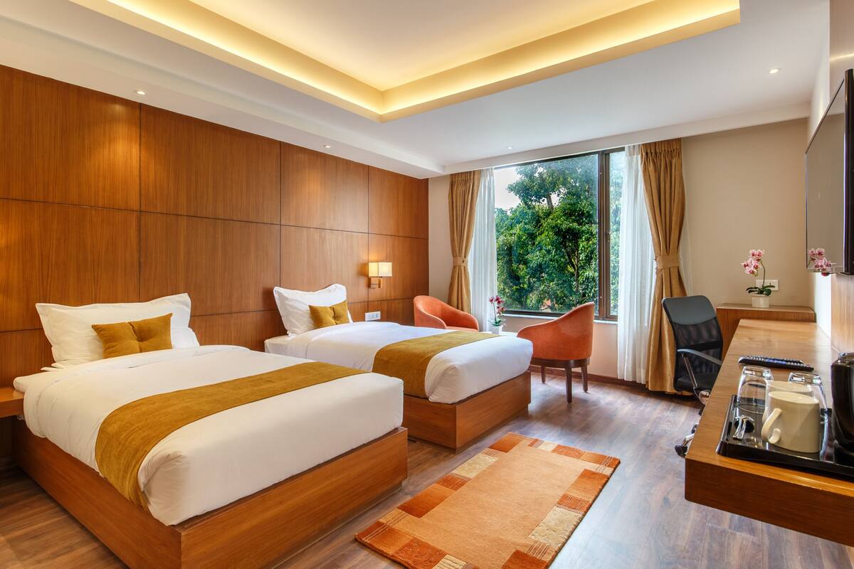 A hotel room with two beds, a desk with a tray, a chair, and a large window with curtains.