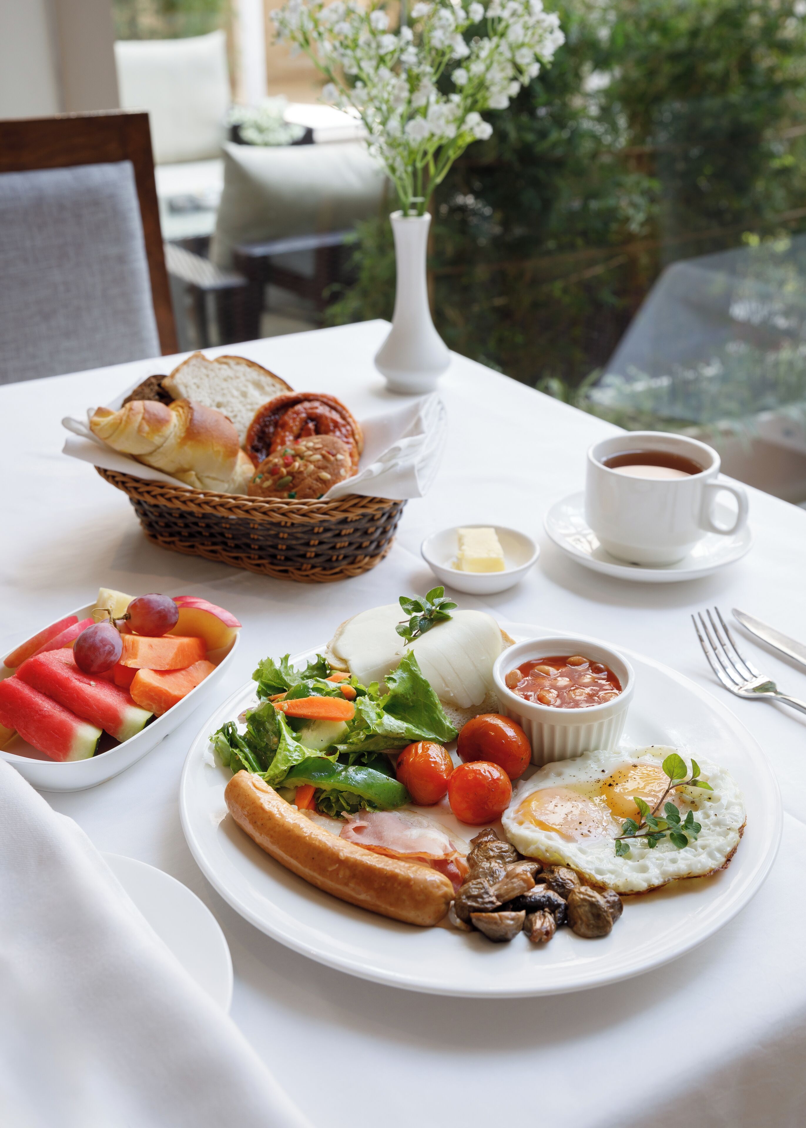 A breakfast table with a variety of food items including bread, fruits, vegetables, eggs, and a cup of coffee.