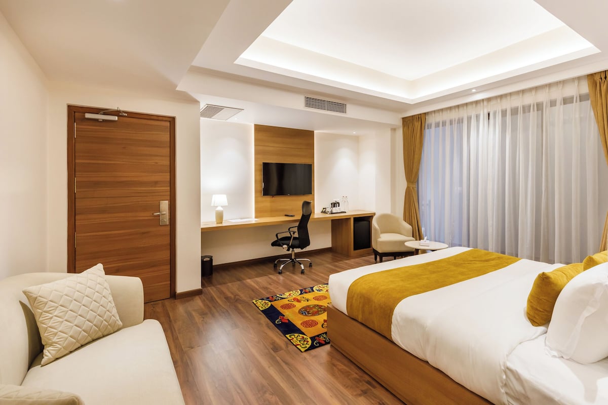 A hotel room with a bed, a desk, a chair, a TV, and a window with curtains.