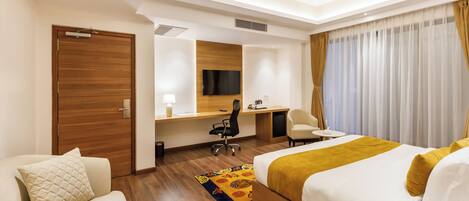 Habitación de hotel con cama, escritorio, silla, televisor y ventana con cortinas.