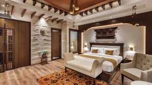 Habitación de hotel con una cama, dos sillas, una mesita pequeña, un detalle decorativo en la pared y techo de madera.