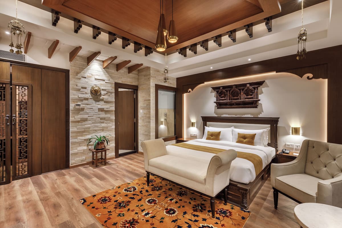 A hotel room with a bed, two chairs, a small table, a decorative wall, and a wooden ceiling.