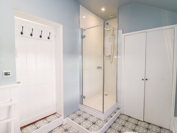 A bathroom with a shower, a white door with hooks, and patterned floor tiles.