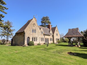 A stone building with a steeply pitched roof and multiple chimneys, surrounded by a grassy lawn and trees.