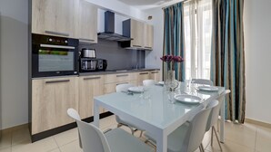 A modern kitchen with a built-in oven, a coffee maker, and a dining table set for six. - Sliema Tigne Suites (Sliema)