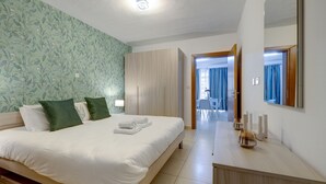 A hotel room with a bed, a wooden wardrobe, a bathroom visible through an open door, and a mirror on the wall. - Sliema Tigne Suites (Sliema)