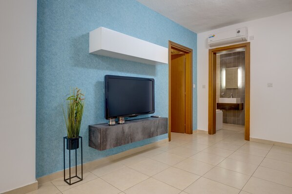 Una sala de estar moderna con un televisor de pantalla plana montado en un mueble gris, una planta en maceta y una pared azul con textura.