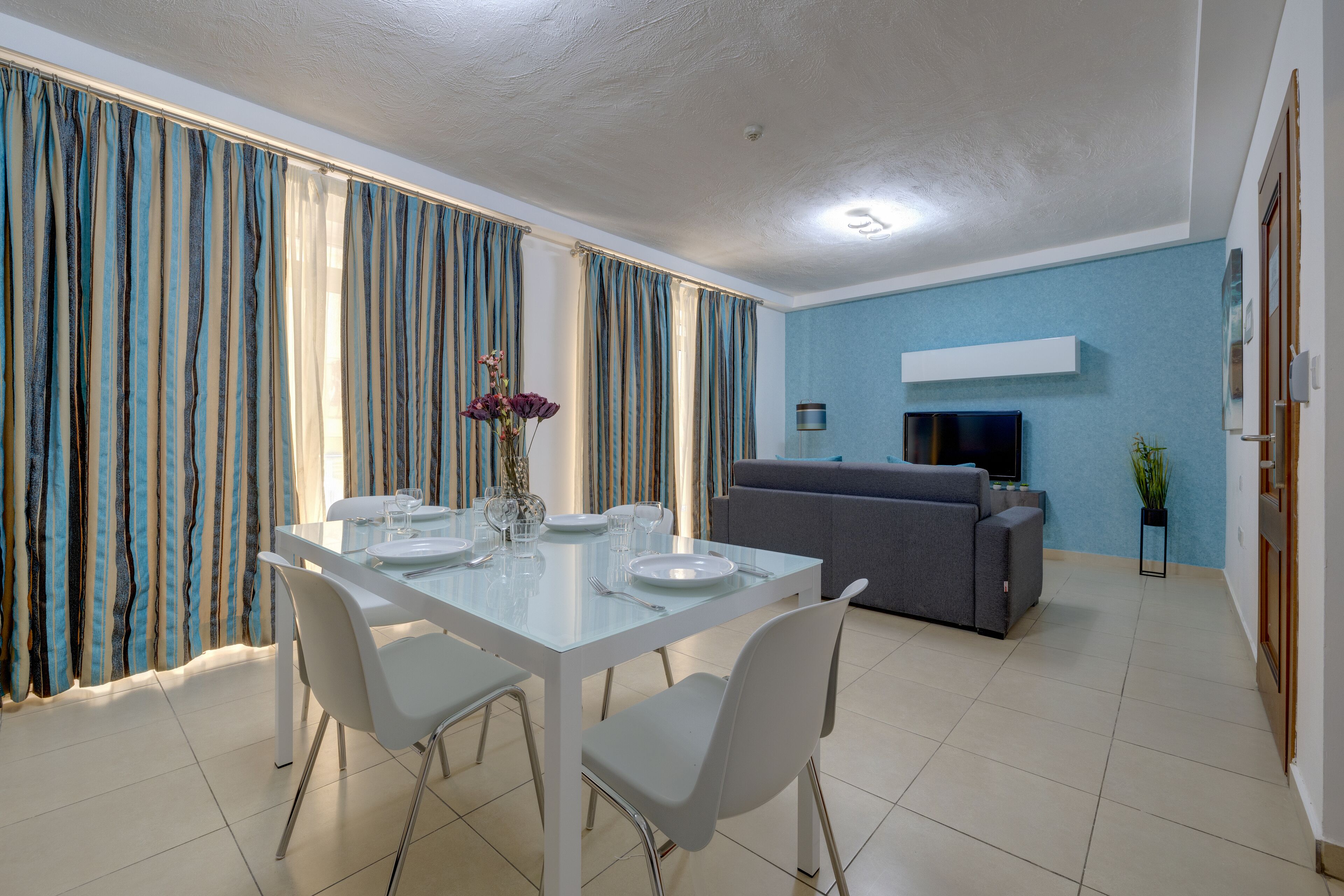 A modern dining area with a white table set for four, a grey sofa, and a blue accent wall.