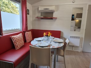 A compact living space with a dining area, a red sofa with patterned cushions, a small table set for two, and a kitchenette in the background.