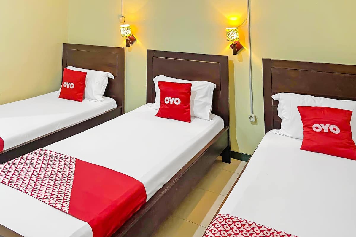 Tres camas individuales con ropa de cama roja y blanca, cada una con un almohadón que lleva el logo de 