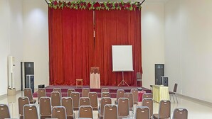 Un salón de conferencias con escenario, cortinas rojas, una pizarra y filas de sillas.