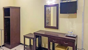 Una habitación con armario, tocador con espejo, televisión de pantalla plana y una pequeña mesa con vasos.