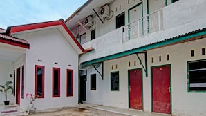 A two-story building with red doors and windows, a balcony, and a potted plant in the entrance. - SPOT ON 91950 Guest House TekNong Syariah (Bangkinang)